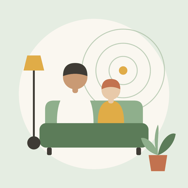 A parent and child sitting together on a green sofa, with a lamp and a plant beside them.